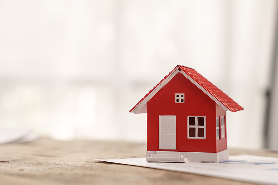 Mortgage Request - Close Up of a Small Red Toy Home Sitting on Top of Documents on a Wooden Table Inside a Brightly Lit Room